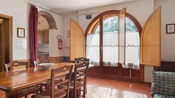 A dining area with a wooden table and chairs, a fire extinguisher, and a view through an arched window.