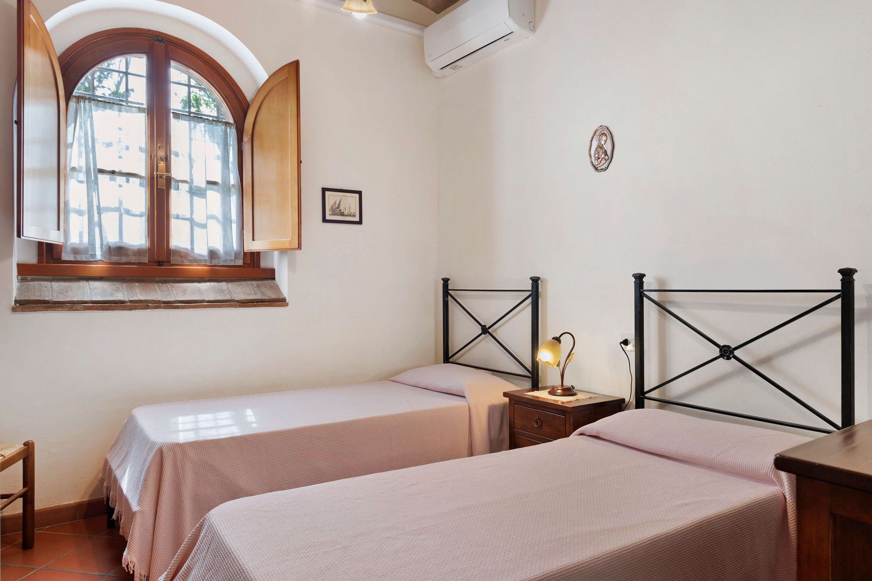 A bedroom with two beds, a window with curtains, a bedside lamp, and a small table.