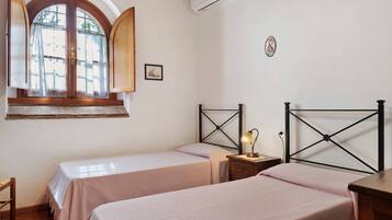 A bedroom with two beds, a window with curtains, a bedside lamp, and a small table.
