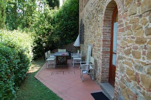 Ein Steinhäuschen mit einer Terrasse, ausgestattet mit Tisch und Stühlen, umgeben von viel Grün.