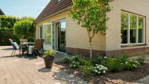 A house with a brick exterior, a small garden with flowers, and a patio with outdoor furniture. - Comfortable country house in Drenthe (Schoonloo)