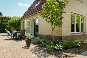 Ein Haus mit Ziegelaußenwand, einem kleinen Garten mit Blumen und einer Terrasse mit Gartenmöbeln.