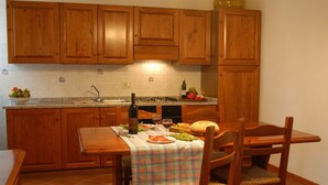 A kitchen with wooden cabinets, a tiled backsplash, a dining table with chairs, and a checkered tablecloth. - Apartment Raffaello: Comfort and Relaxation with Private Outdoor Space (Montaione)
