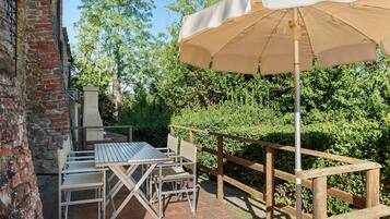 Un patio al aire libre con una mesa, sillas, un cerramiento de madera y un paraguas grande.