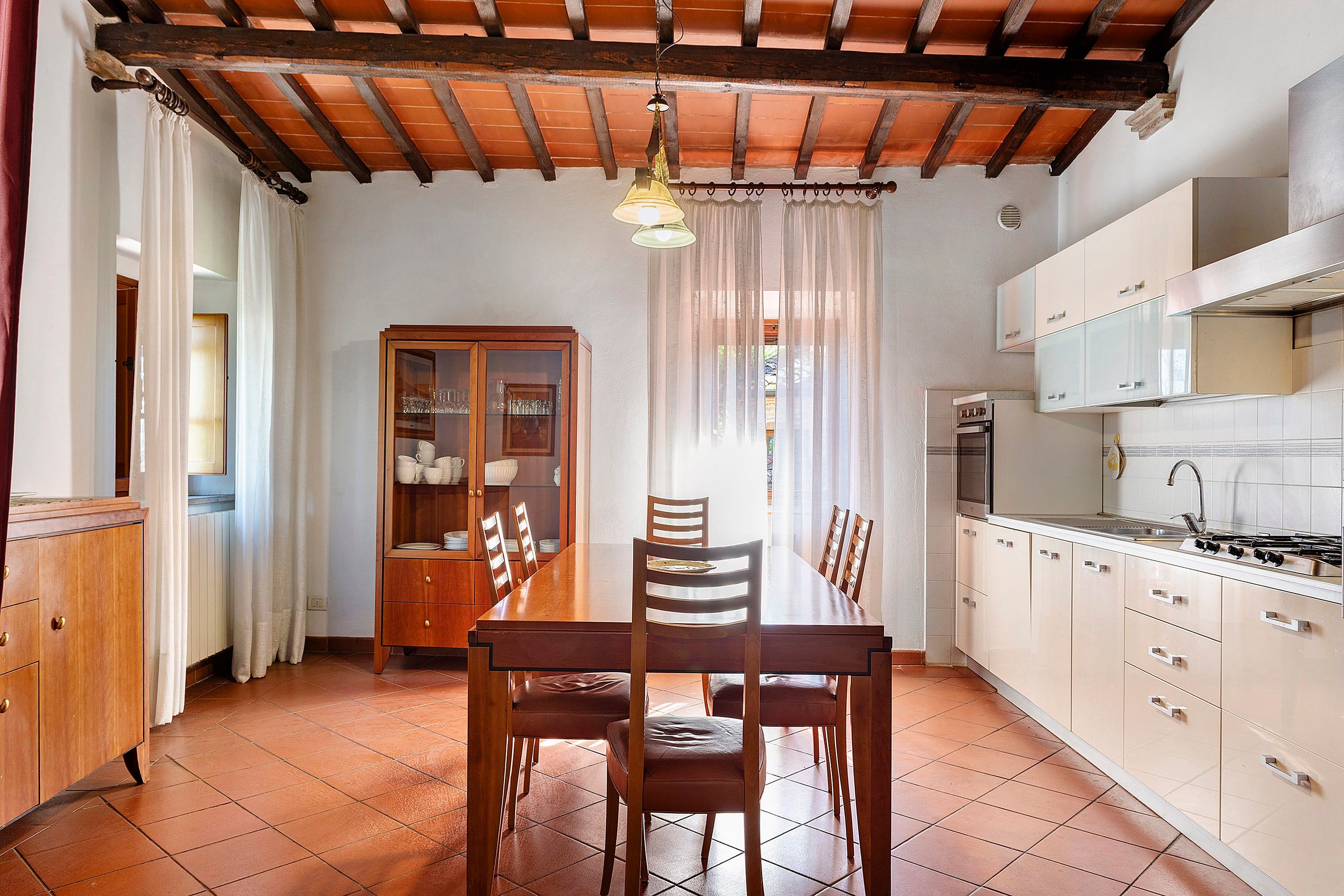 Una cocina con mesa y sillas, un armario con puertas de cristal y suelo de baldosas.