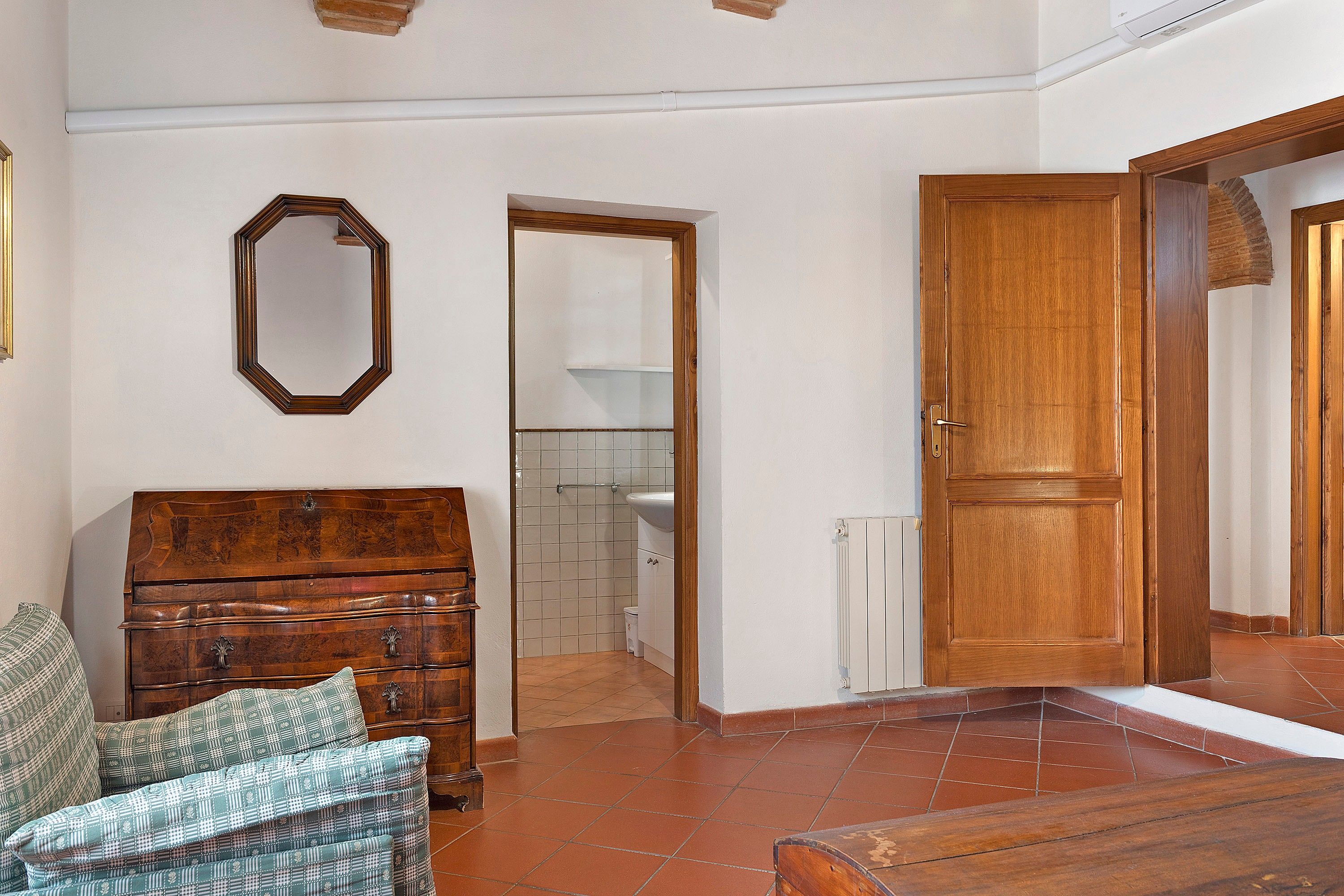 Una habitación con un armario de madera, un espejo, una puerta y suelo de baldosas.
