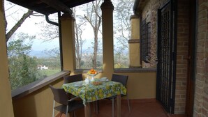 Un balcón con una mesa dispuesta para dos personas, sillas, mantel y vistas del paisaje.