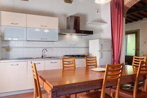 A kitchen with white cabinets, a gas stove, and a dining table with chairs. - Michelangelo Apartment: Panoramic Views & Spacious Comfort (Montaione)