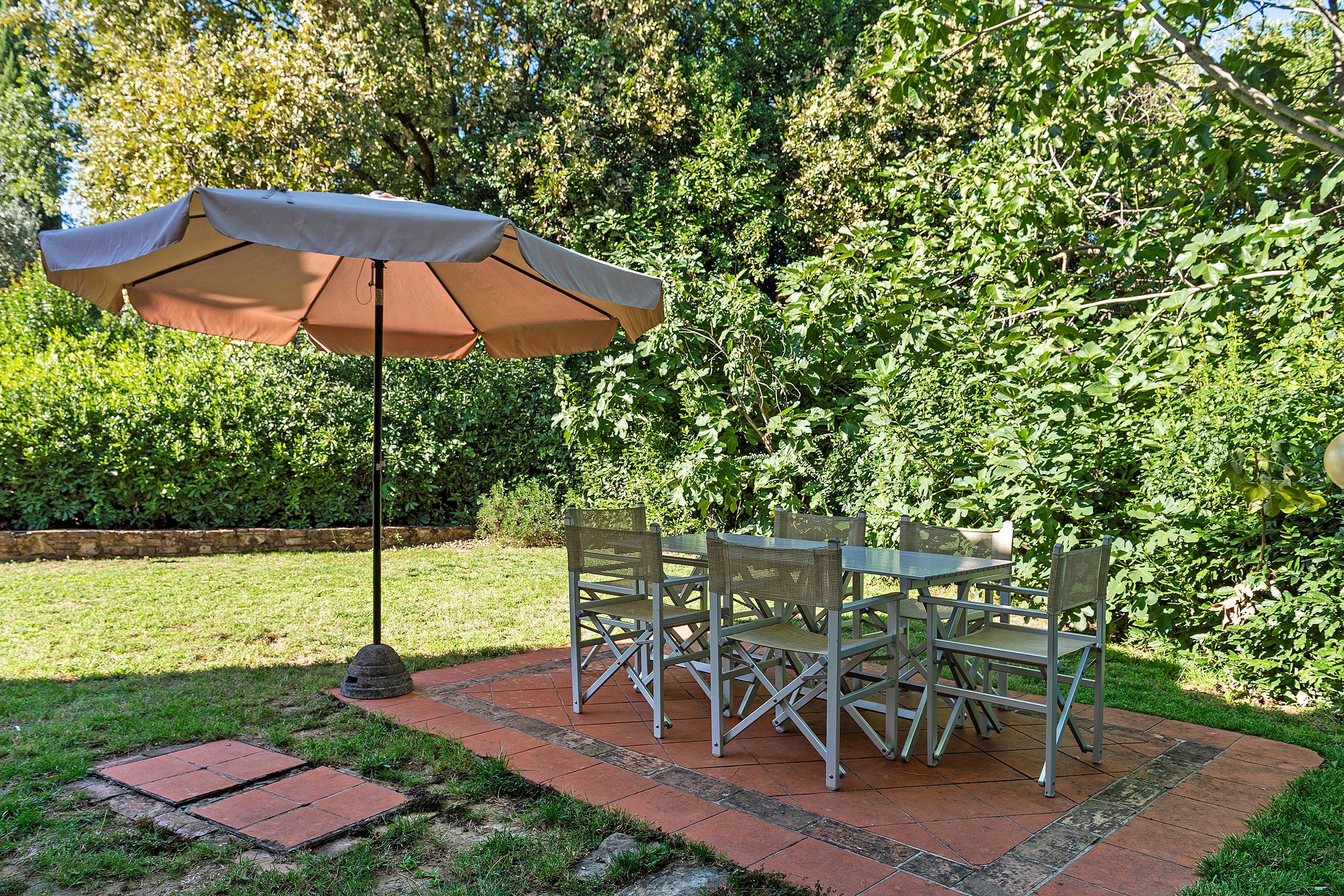 An outdoor patio with a table and chairs, a single umbrella, and a brick pathway.