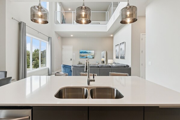 A modern kitchen with a large island, stainless steel sink, and pendant lighting. - Skyline Luxe Retreat  Loft, Pool Table & Rooftop Balcony Near Disney (Kissimmee)