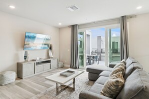 A living room with a sofa, a coffee table, a TV, and a sliding glass door leading to an outdoor area. - Skyline Luxe Retreat  Loft, Pool Table & Rooftop Balcony Near Disney (Kissimmee)