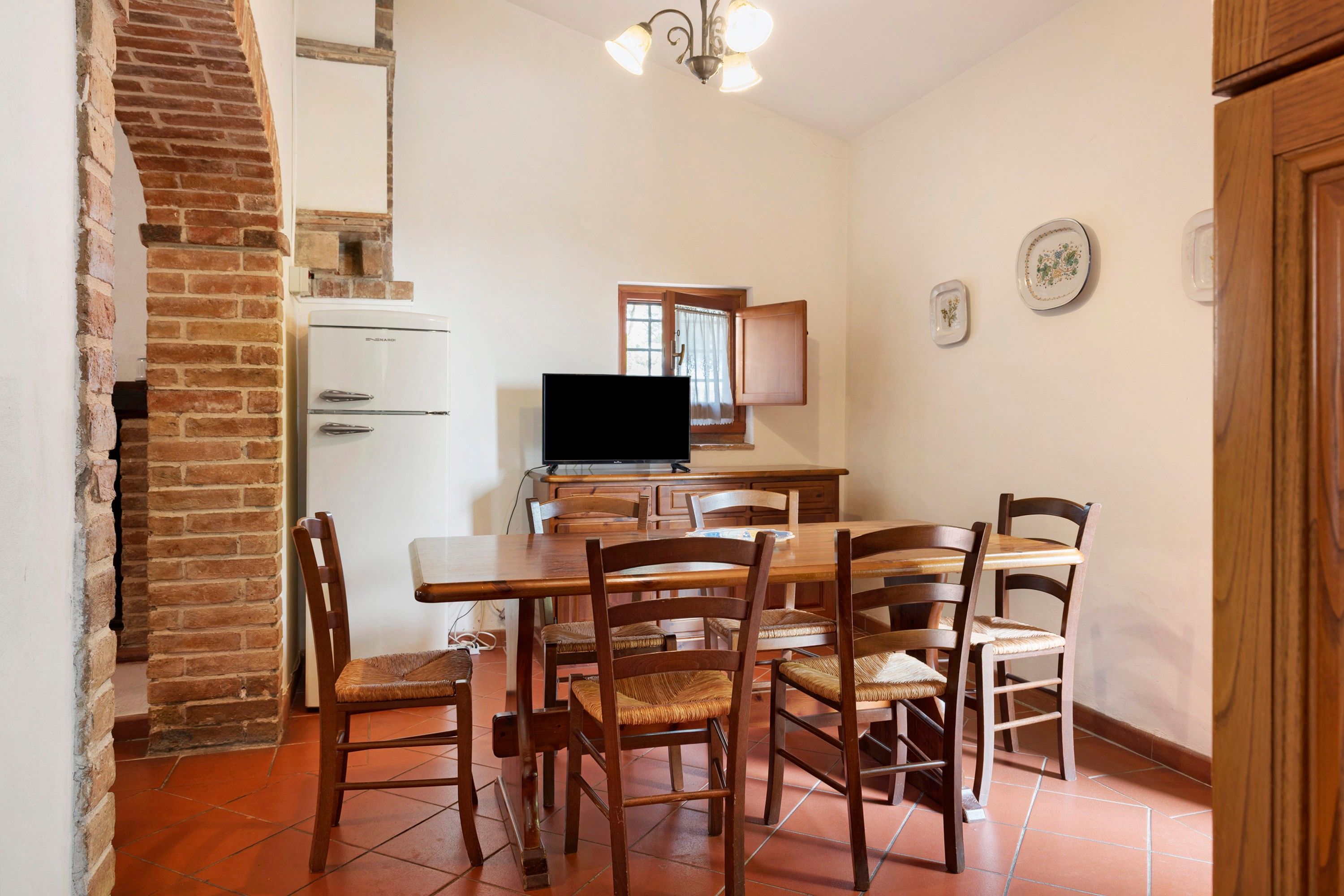 A dining area with a brick wall, a television, and a wooden table with chairs.