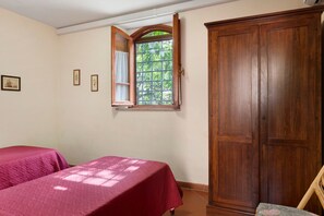 Een kamer met twee bedden, een houten garderobe en een raam met uitzicht op groen.