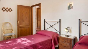 Ein Schlafzimmer mit Holztür, einem Bett mit Metallgestell, einem Nachttisch mit Lampe, einem Stuhl und einem Wandbild.