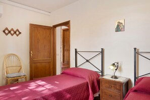 Een slaapkamer met een houten deur, een bed met metalen frame, een nachtkastje met een lamp, een stoel en een aan de muur bevestigd schilderij.