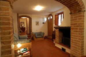 A cozy living room with a fireplace, a sofa, a wicker table with books, and a door leading to another room. - Donatello Apartment: Relaxation and Comfort in Montaione (Montaione)