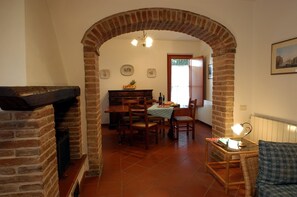 A dining area with a brick archway, wooden furniture, a table with a checkered tablecloth, and a wicker chair. - Donatello Apartment: Relaxation and Comfort in Montaione (Montaione)