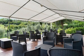 Een terras met overkapping, rieten meubilair en uitzicht op groen.