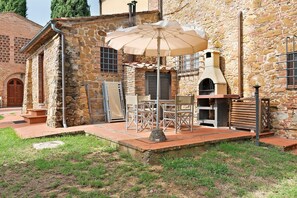 Ein Steinhaus mit einer Terrassenanlage, die Gartenmöbel und einen Grill umfasst.