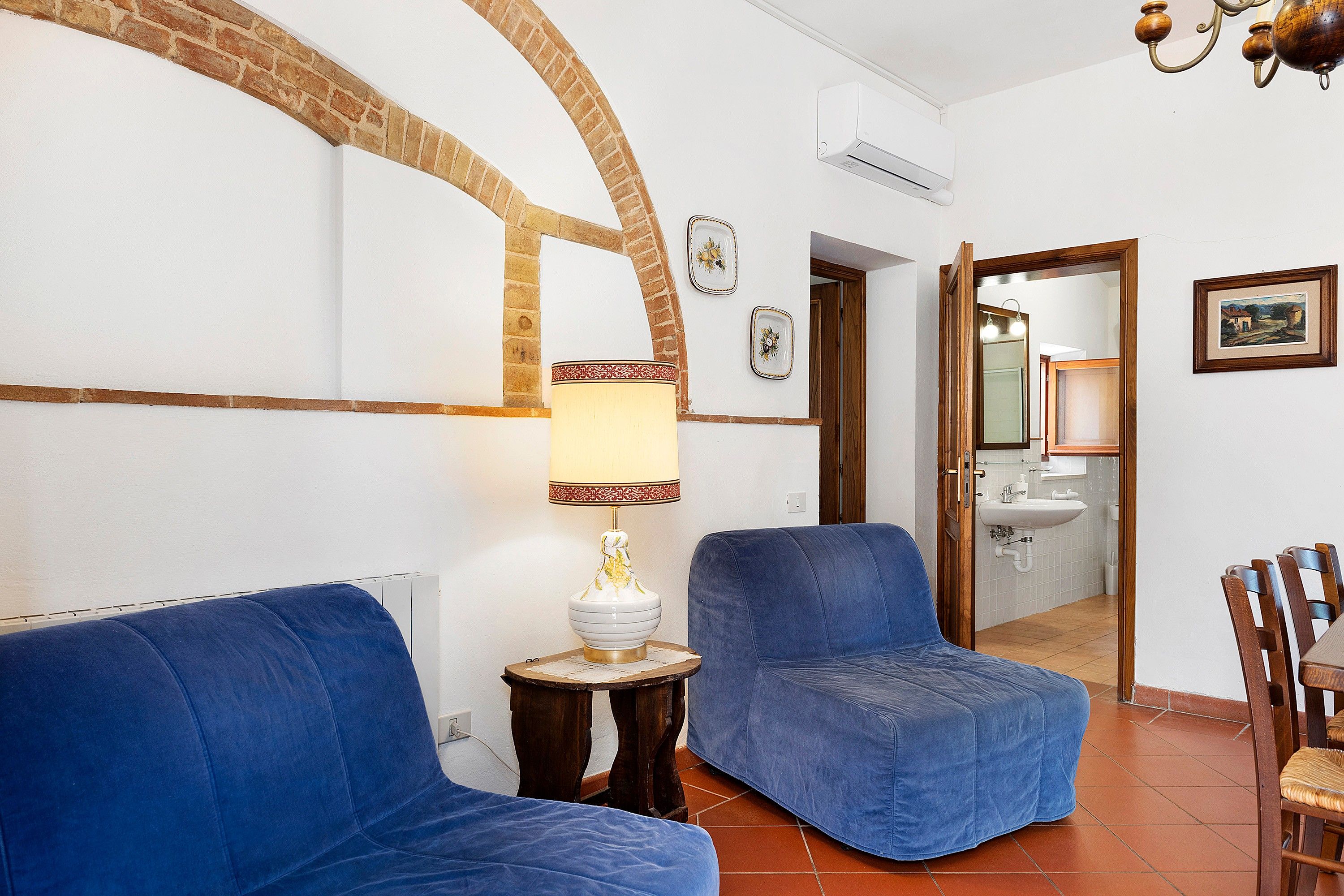 Une pièce avec deux canapés bleus, une petite table avec une lampe, un miroir et un tableau encadré accroché au mur.