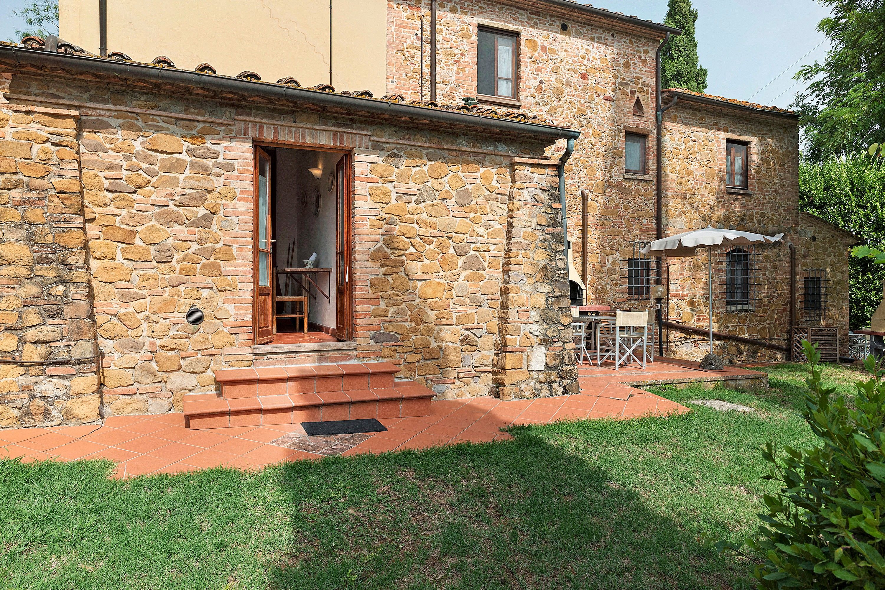 A stone building with a wooden door and steps leading to a covered outdoor seating area.