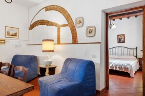 Ein Zimmer mit zwei blauen Sesseln, einem kleinen Tisch mit Lampe, einem Bett mit weißer Bettdecke und einer Wand mit dekorativem Bogen und gerahmten Bildern.