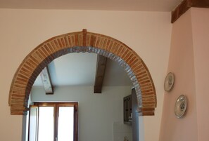 Ein rundbogiger Ziegelbogen führt in einen Raum mit weißer Wand und einer Tür.