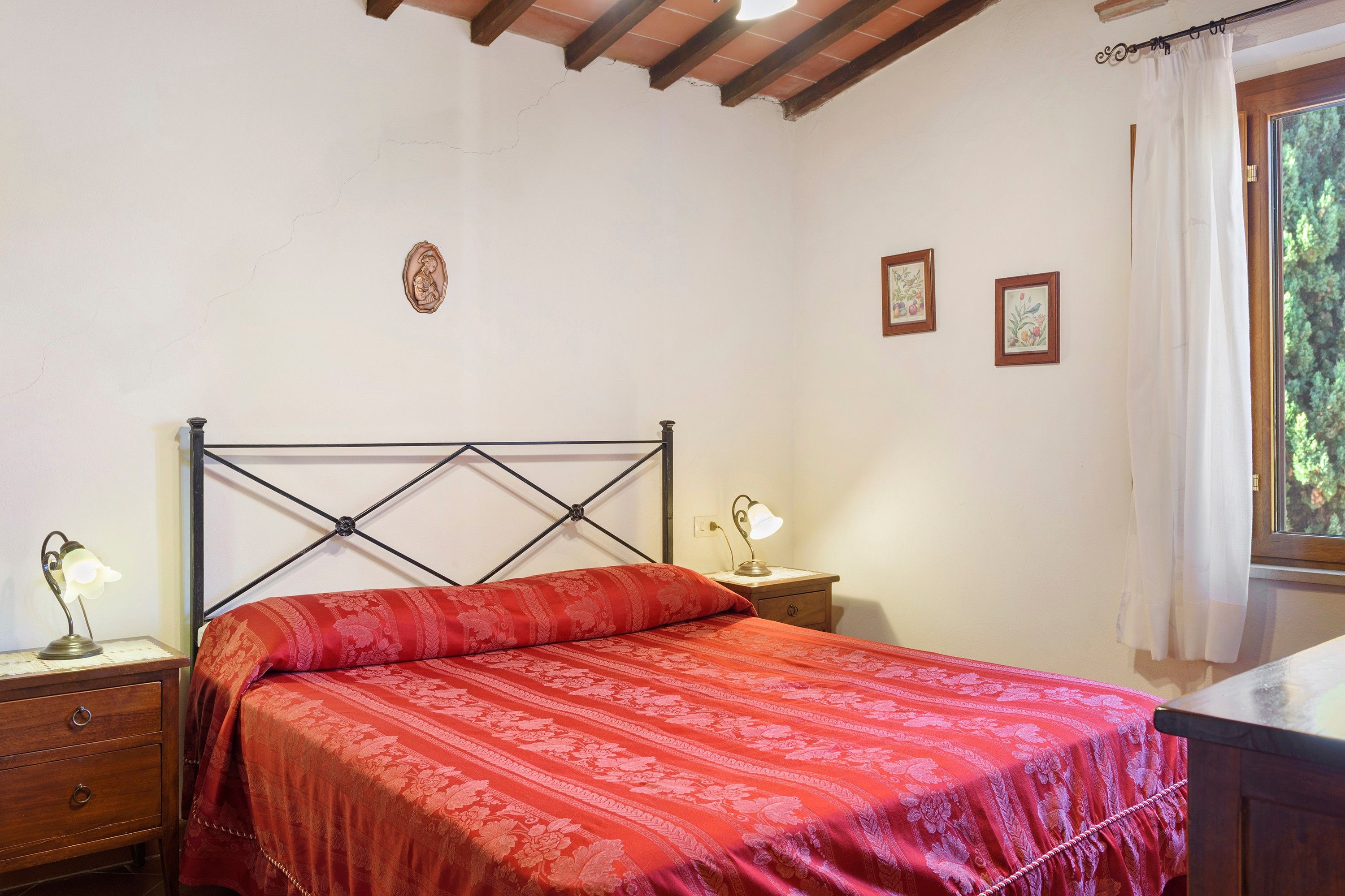 Un dormitorio con una cama, una mesita de noche, una lámpara y una ventana con cortinas.