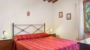 Un dormitorio con una cama, una mesita de noche, una lámpara y una ventana con cortinas.