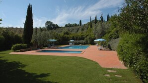 Un jardín ajardinado con piscina, sillas de descanso y sombrillas.