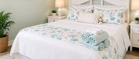 A bedroom with a bed, nightstands, a potted plant, and a wall-mounted painting.