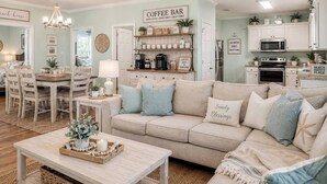 Un salon chaleureux avec un canapé beige, un coin bar et un espace repas comprenant une table et des chaises en bois.