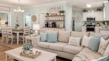 Una sala de estar acogedora con un sofá color beige, una barra para café y una zona de comedor con mesa y sillas de madera.