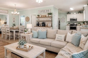 Ein gemütliches Wohnzimmer mit einem beigefarbenen Sofa, einer Kaffeebar und einem Essbereich mit Holztisch und Stühlen.