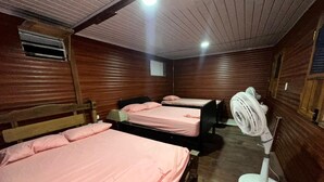 Una habitación con tres camas, cada una con ropa de cama rosa, cabeceras de madera y un ventilador.