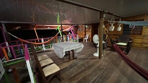 Una terraza de madera con una mesa, sillas, una hamaca y un ventilador.