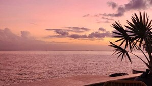 Blick auf das Meer mit einer Speisekarte auf dem Tisch, Palmen und einem Sonnenuntergang.