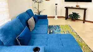 Ein Wohnzimmer mit einem blauen Ecksofa, einem Flachbildfernseher, einer Wandverkleidung und einer Stehlampe.