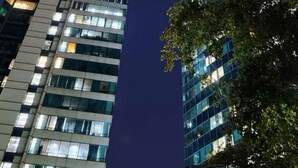 Zwei hohe Gebäude mit beleuchteten Fenstern vor dunklem Himmel.