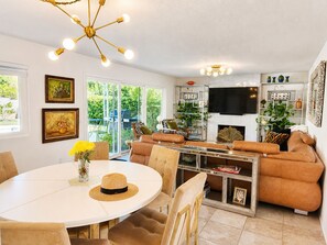 Ein modernes Wohnzimmer mit einem weißen Esstisch, einem braunen Ledersofa und einem an der Wand befestigten Fernseher.