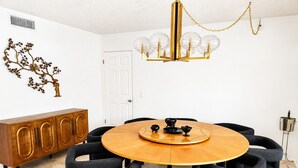 Una sala da pranzo con un tavolo rotondo in legno, sedie nere, un lampadario dorato e un armadietto in legno.