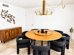 Ein Esszimmer mit einem runden Holztisch, schwarzen Stühlen, einer goldfarbenen Chandelieber und einem Holzkabinett.