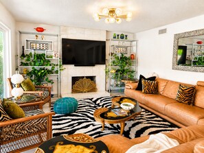 Una sala de estar con un sofá, sillones, una mesa de centro, chimenea y estanterías con plantas y objetos decorativos.
