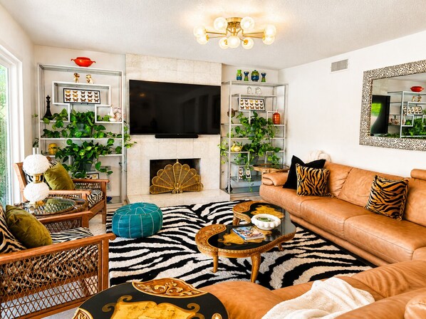 Una sala de estar con un sofá, sillones, una mesa de centro, chimenea y estanterías con plantas y objetos decorativos.