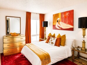 Una habitación de hotel con cama, cómoda, espejo, cuadro y lámpara.
