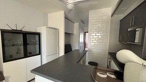 Une cuisine moderne dotée d’un îlot central, de meubles blancs et d’un four à micro-ondes encastré.