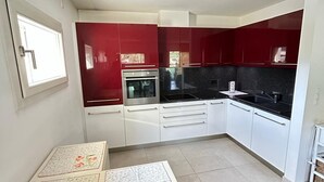 Une cuisine moderne avec des meubles rouges et blancs, un plan de travail noir et un sol carrelé.