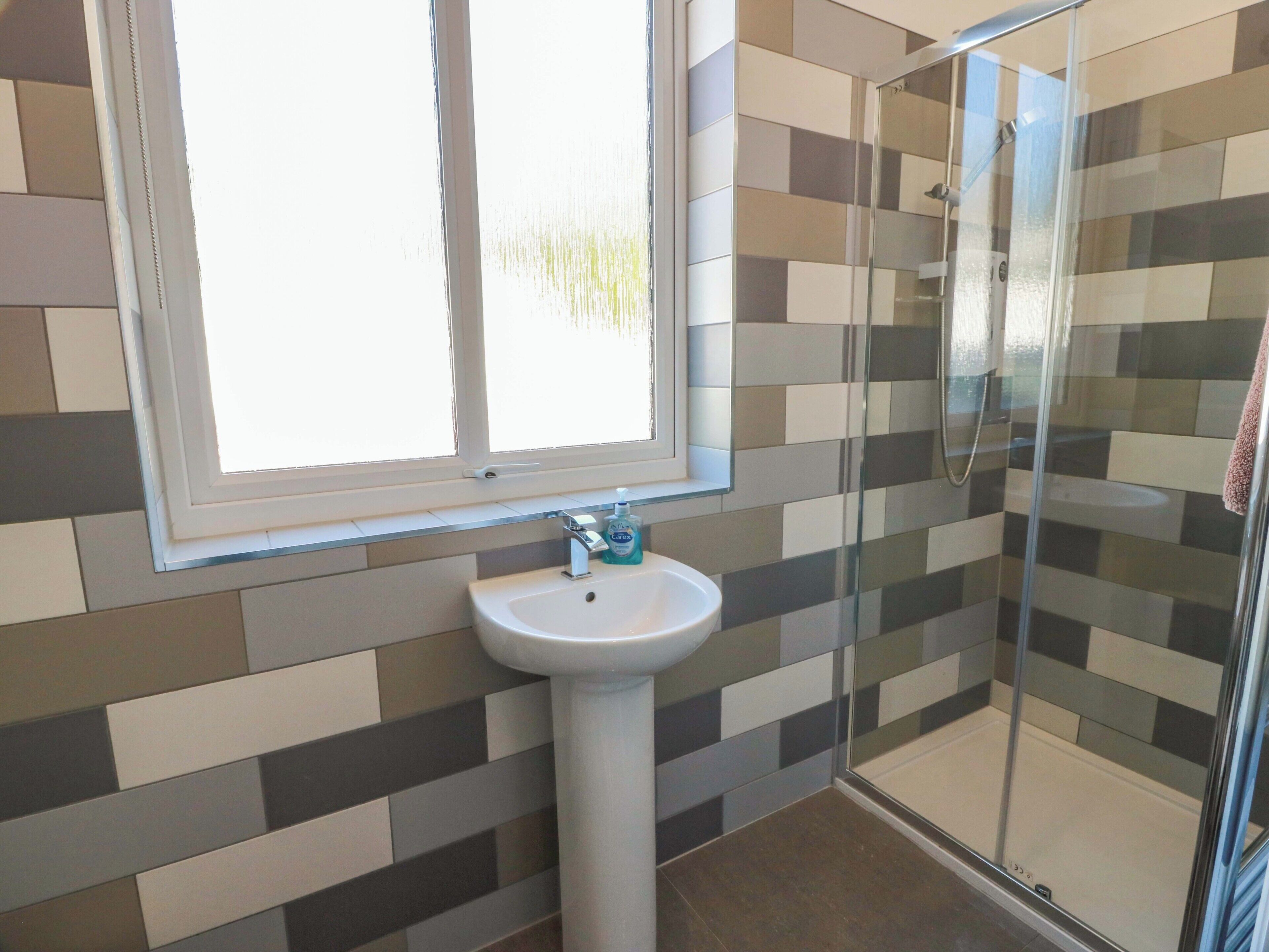Une salle de bain avec une fenêtre, un lavabo et un espace douche.