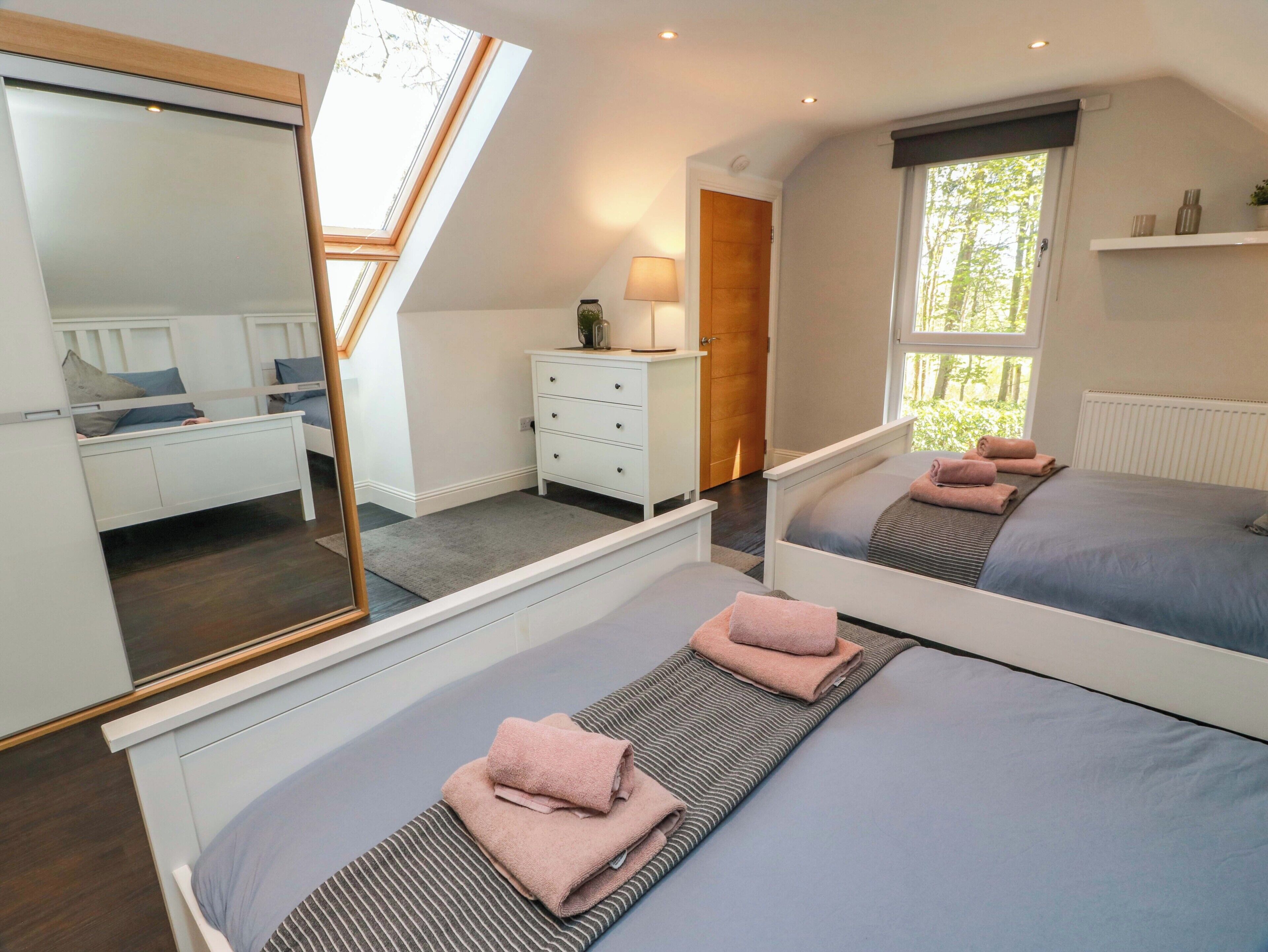 A bedroom with two beds, a dresser, a mirror, and a window with a view.