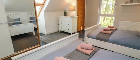 A bedroom with two beds, a dresser, a mirror, and a window with a view.
